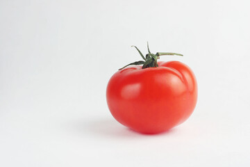 Red ripe tomato on a white background. The tomato has a green tail