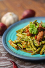 Stir fried pork belly and red curry paste with sting bean served in a blue plate on a wooden table.