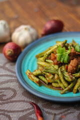 Stir fried pork belly and red curry paste with sting bean served in a blue plate on a wooden table.