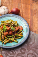 Stir fried pork belly and red curry paste with sting bean served in a blue plate on a wooden table.