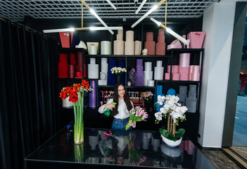 Naklejka premium A young female florist takes care of flowers in a cozy flower shop and collects bouquets. Floristry and making of buckets in a flower shop. Small business.