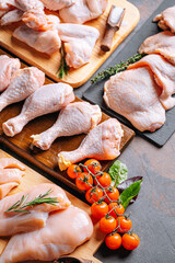 Prepared for frying, butchered various portions of raw chicken meat. Set of raw chicken fillet, thigh, wings, strips and legs on the background of the culinary table with spices and cherry tomatoes