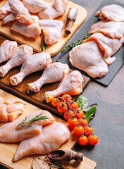 Prepared for frying, butchered various portions of raw chicken meat. Set of raw chicken fillet, thigh, wings, strips and legs on the background of the culinary table with spices and cherry tomatoes