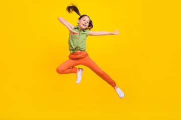 Foto eines fröhlichen, aufgeregten, jugendlichen Mädchens, gekleidet in grünes Oberteil, springend, hoch tanzend, lächelnd, isolierter gelber Farbhintergrund