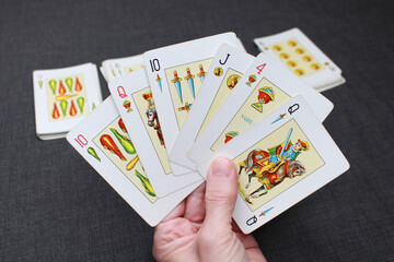 A hand holding a deck of Spanish-suited cards. In the background, more cards from the deck are shown. Colors: black, white and yellow.