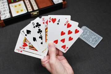 A hand shows a deck with different poker cards. In the background, you can see different cards from the game and a briefcase of board games. Perfect to use as a colorful wallpaper.