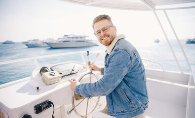 Portrait smile happy man driver captain of white luxury yacht holding helm wheel, summer travel on...