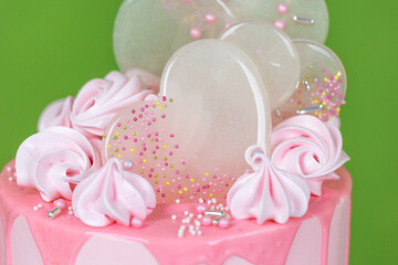 Pink cream cheese cake with chocolate chip gouges decorated with meringues and isomalt lollipops. Beautiful delicious birthday cake on the green background. Picture for a menu 