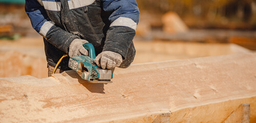 Industrial work carpenter grinds log with electric jointer, construction frame building site of house made of wood