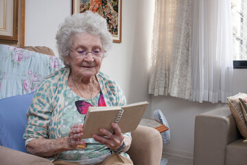 Elderly Lady at home sitting in a chair reading a Book 