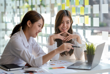Two Smiling young Asian businesswoman talking to colleague, employees brainstorming, sitting working at office