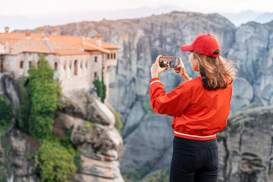 Tourist girl taking photos on smartphone of the scenic Meteora Monstery of Varlaam near Kalabaka town. Sightseeing and travel blogger concept