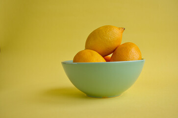 large lemons in a deep turquoise vase on a yellow background