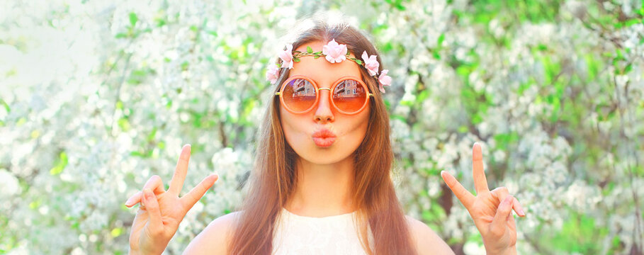 Portrait of beautiful young woman and flowers wearing floral headband, sunglasses on spring blooming garden background