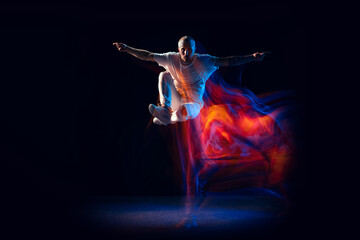 Obraz premium Jumping. Stylish man in sports white outfit dancing hip-hop, breakdance isolated on dark background in mixed neon light. Youth culture, hip-hop, style and fashion, action.