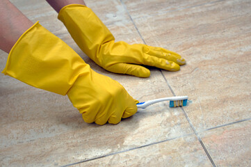 Cleaning tile joints with a toothbrush. Yellow household gloves.