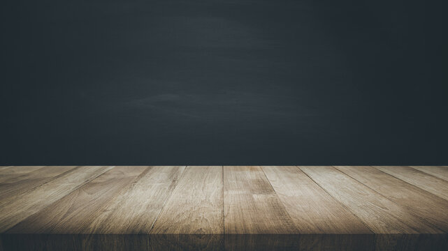 Selective focus of wood table top on blur dark blackboard background.
