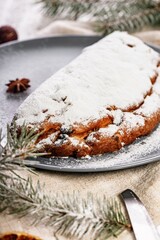 Christmas stollen on a gray plate. Wooden white table background. Traditional Christmas pastry with marzipan, nuts and raisins. Close-up. Vertical shot