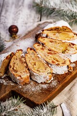 Christmas stollen on a cutting board. Wooden white table background. Traditional Christmas pastry with marzipan, nuts, raisins and dried fruit. Vertical shot
