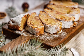 Christmas stollen on a cutting board. Wooden white table background. Traditional Christmas pastry with marzipan, nuts, raisins and dried fruit.