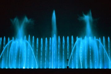 Beautiful fountain show. Large multi colored decorative dancing water jet led light fountain show at night. Dark background.