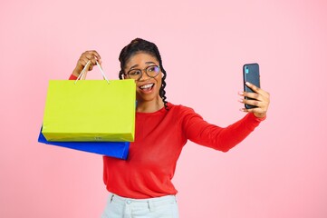 Young black woman holding shopping bags on pink backgrond