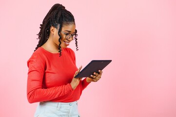 Young american student girl with curly african hair holding digital tablet and smiling standing over isolated pink background with copy space for text, logo or advertising. - Powered by Adobe