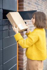 Young woman getting parcel from cell of automatic post terminal outdoors. Concept of contactless...
