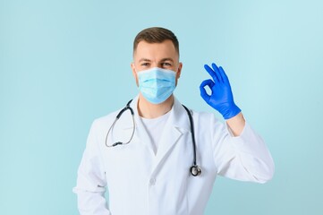 Young male doctor wearing medical mask, and stethoscope round his neck, isolated on blue background