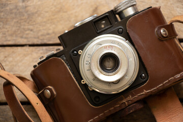 Old photo camera in a leather case and a wooden table close up