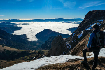 Naklejka na ściany i meble A man enjoying the panoramic view from mount Eisenerzer Reichenstein in Styria, Austria, Europe. The Ennstal valley is covered in clouds and fog.Hiking trail,Wanderlust. Sunny day.Freedom concept