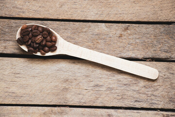 roasted coffee grains in a wooden spoon on an old wooden table
