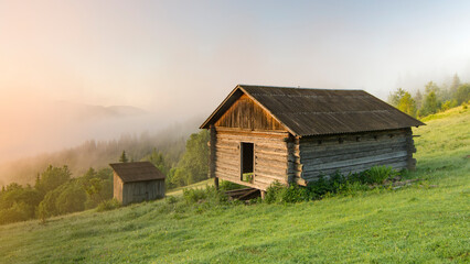 Old wooden house on the hill. Beautiful morning in the Carpathians. Fog and haze on the tops of the mountains.