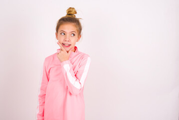 caucasian little kid girl with bun hairstyle wearing pink tracksuit over white background Thinking worried about a question, concerned and nervous with hand on chin.