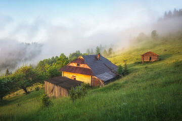 Old wooden house in the mountains. Beautiful morning in the Carpathians. Fog and haze on the tops of the mountains.