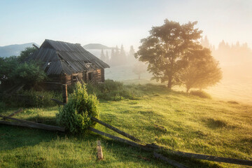 Old wooden hut in the mountains. Beautiful sunrise in the mountains. Fog and haze on the tops of...