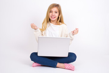 Fototapeta premium caucasian teen girl sitting with laptop in lotus position on white background , making money gesture.