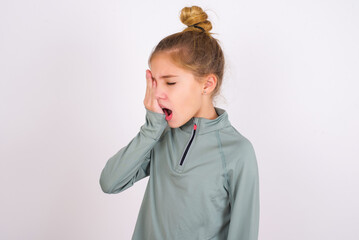 little caucasian kid girl with hair bun wearing technical shirt over white background Yawning tired...