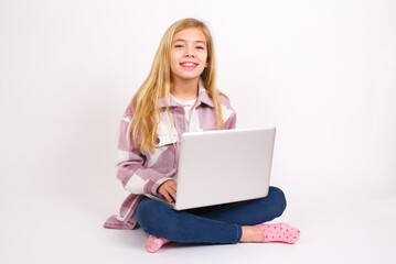 Fototapeta premium caucasian teen girl sitting with laptop in lotus position on white background with happy and funny face smiling and showing tongue.