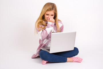 caucasian teen girl sitting with laptop in lotus position on white background , holding his nose because of a bad smell.