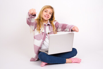 Portrait of charming caucasian teen girl sitting with laptop in lotus position on white background , smiling broadly while holding hands over her head.  Confidence and relax concept.