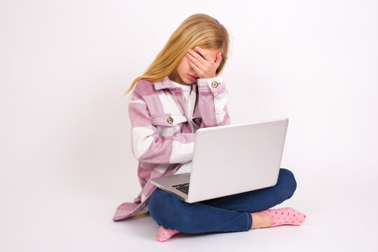 Caucasian Teen Girl Sitting With Laptop In Lotus Position On White Background Making Facepalm Gesture While Smiling Amazed With Stupid Situation.