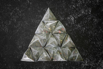 Set of tea bags-pyramids with green flavored tea, on a dark textured surface of the kitchen table. Pyramid shape