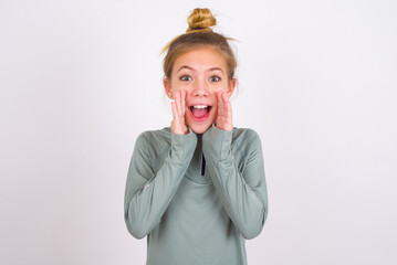 little caucasian kid girl with hair bun wearing technical shirt over white background shouting excited to front.
