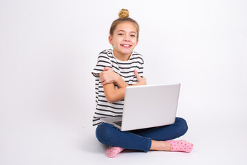 Charming pleased caucasian teen girl sitting with laptop in lotus position on white background embraces own body, pleasantly feels comfortable poses. Tenderness and self esteem concept