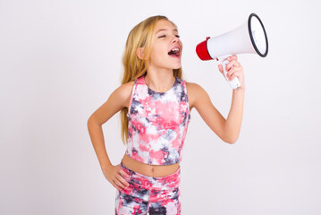 Funny little caucasian kid girl wearing sport clothing over white background People sincere emotions lifestyle concept. Mock up copy space. Screaming in megaphone.