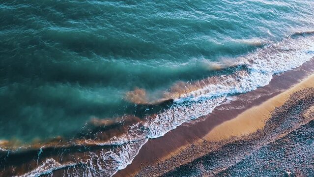 Plano a&eacute;reo de oleaje en la playa del mar mediterr&aacute;neo con tonos de aguamarina verde y azul espuma y arena marr&oacute;n con piedras