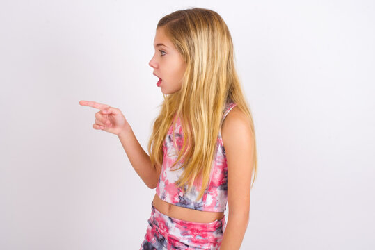 Stunned little caucasian kid girl wearing sport clothing over white background with greatly surprised expression points away on copy space, indicates something
