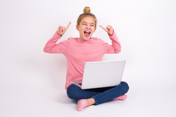 Photo of crazy Beautiful caucasian teen girl sitting with laptop in lotus position on white background screaming and pointing with fingers at hair closed eyes