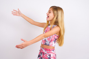 Funny astonished little caucasian kid girl wearing sport clothing over white background look empty space with arms opened ready to catch something.